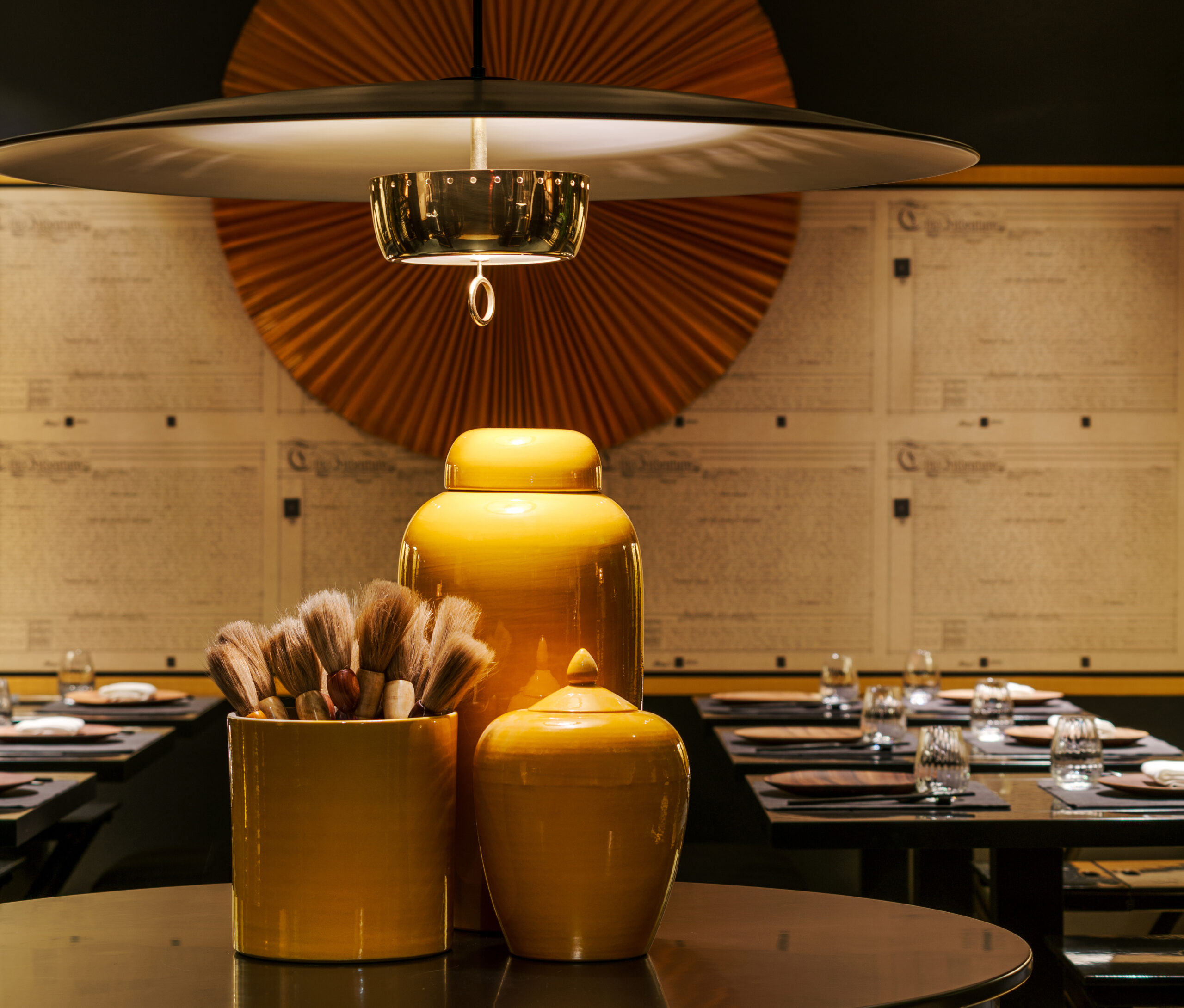 Elegant table setting at Yellow Pot Tanjong Pagar featuring yellow ceramic canisters, calligraphy brushes, and warm ambient lighting.